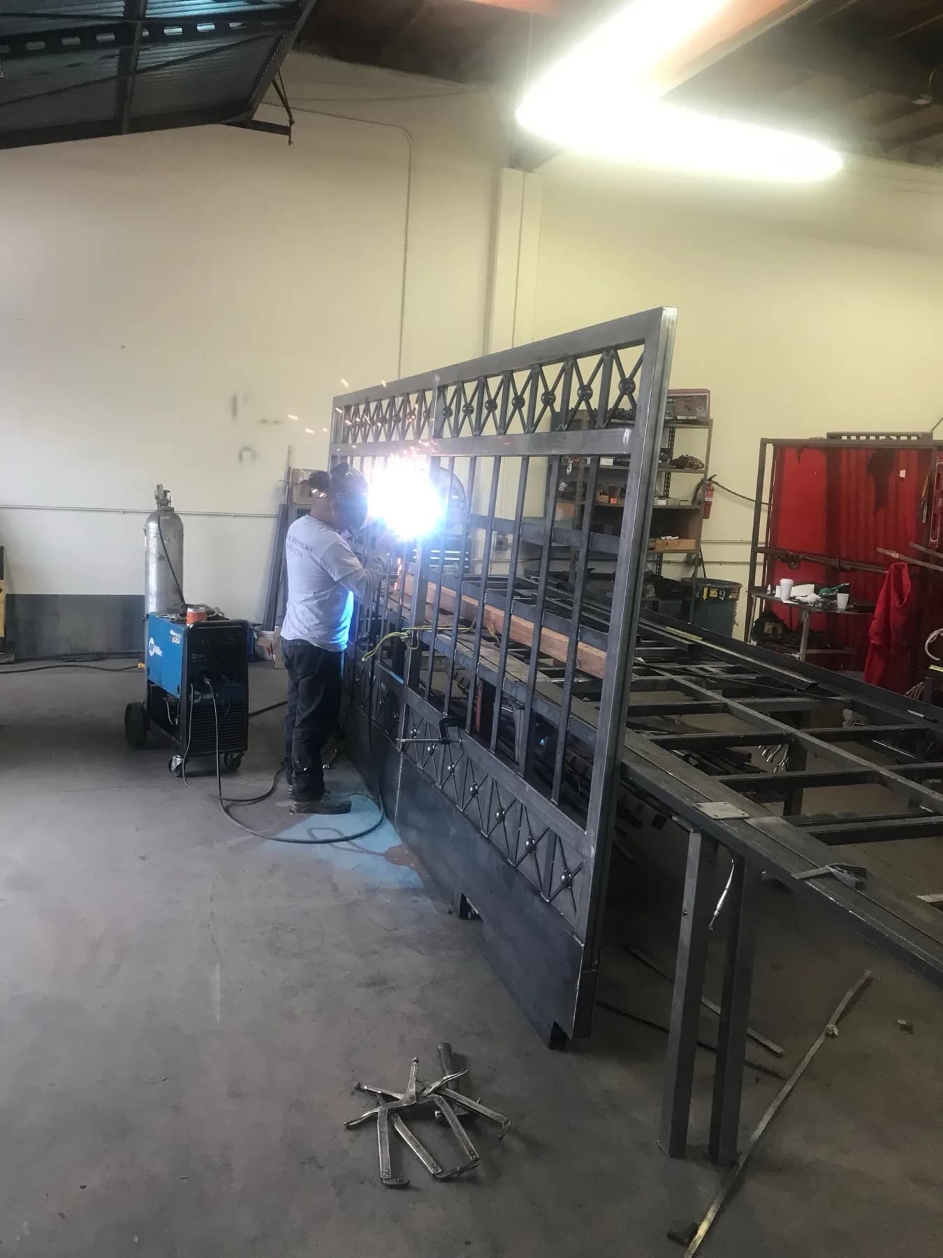 Welder fabricating a large ornamental metal gate panel in the Fence Menders shop