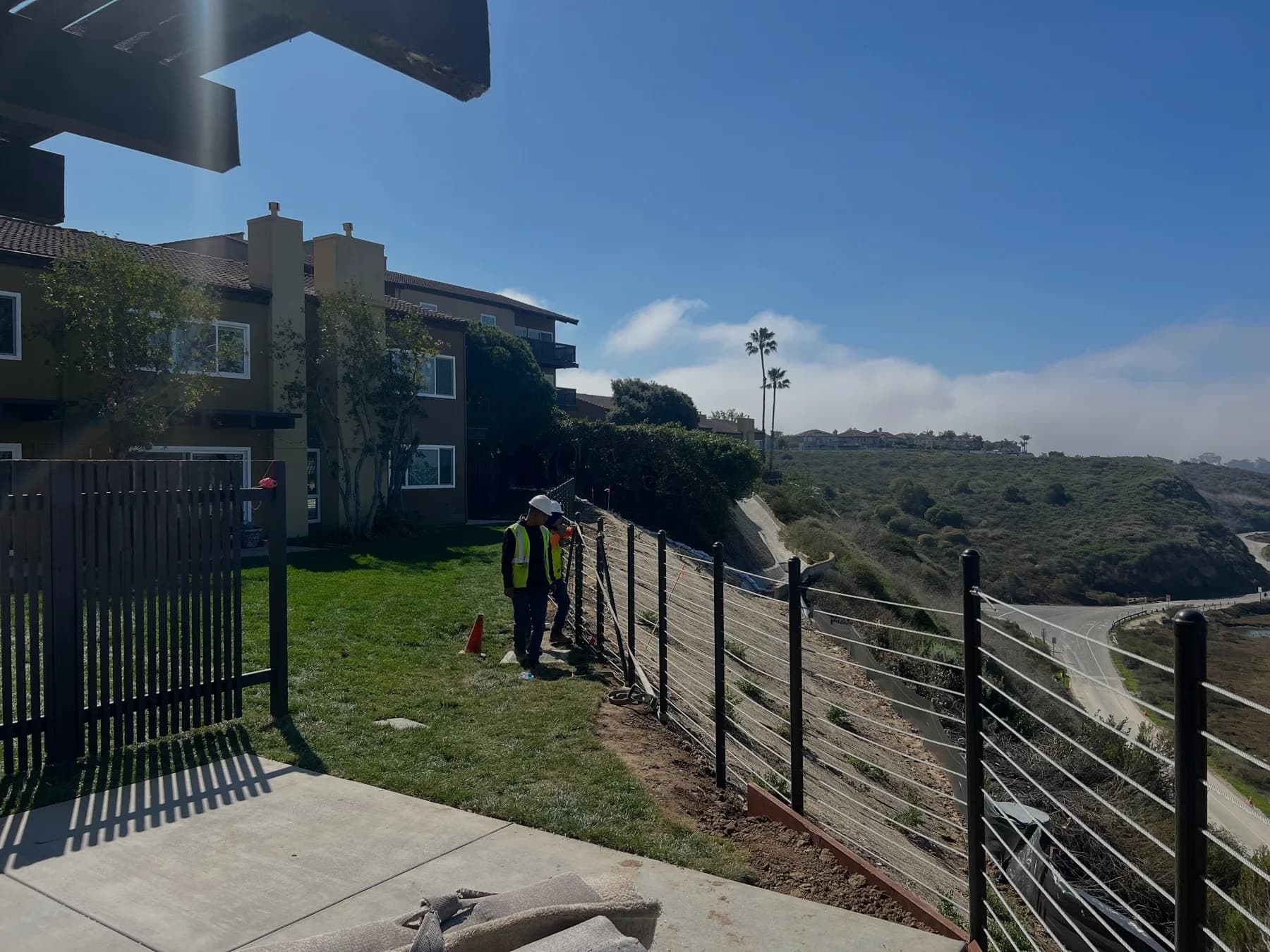 Worker installing a horizontal cable barrier along a landscaped slope