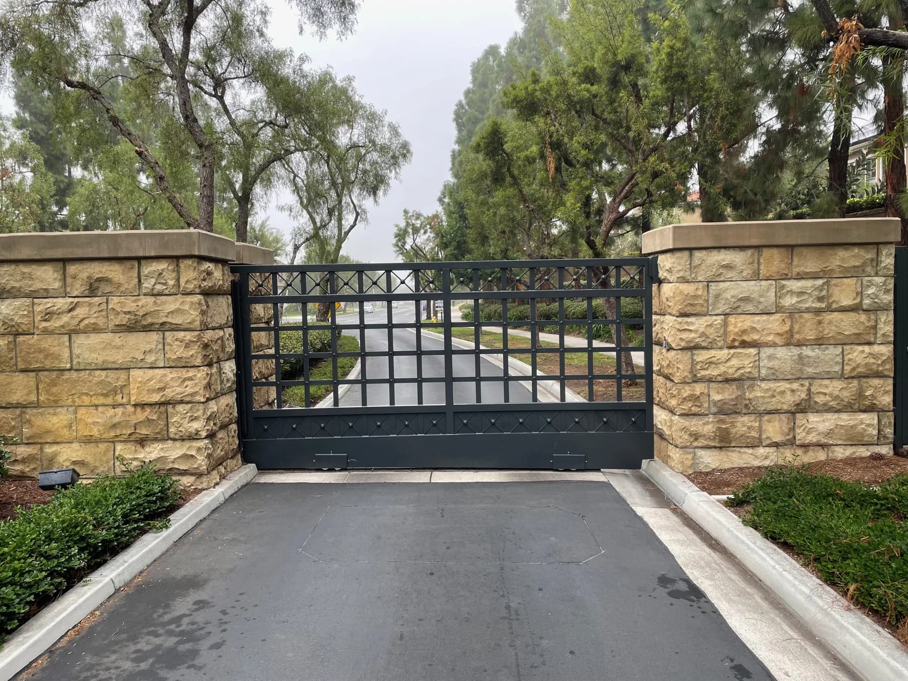 Black ornamental metal swing gate between masonry driveway columns
