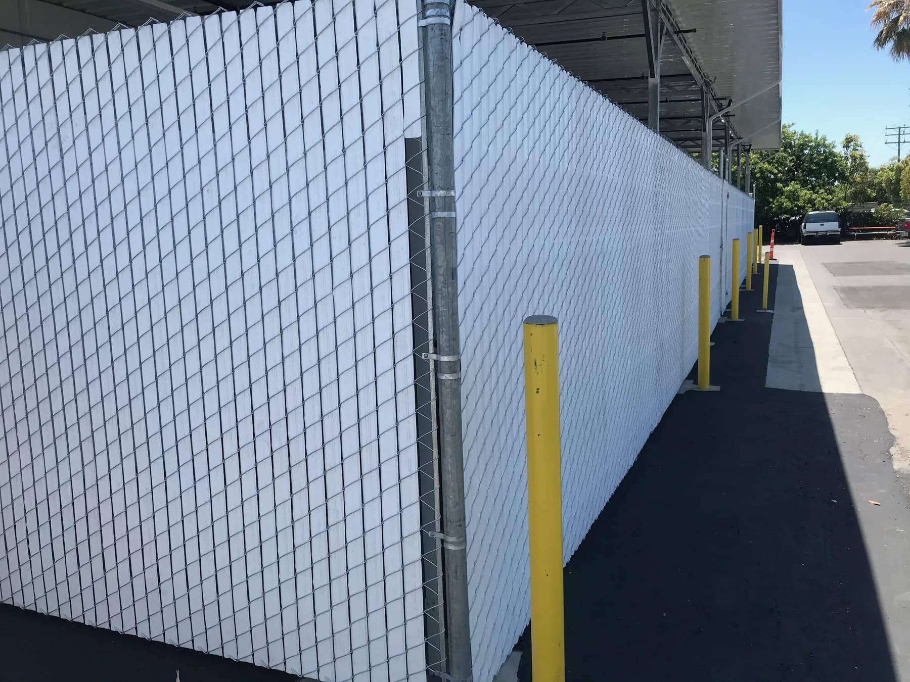 Chain-link service enclosure with white privacy infill, an access gate, and protective bollards