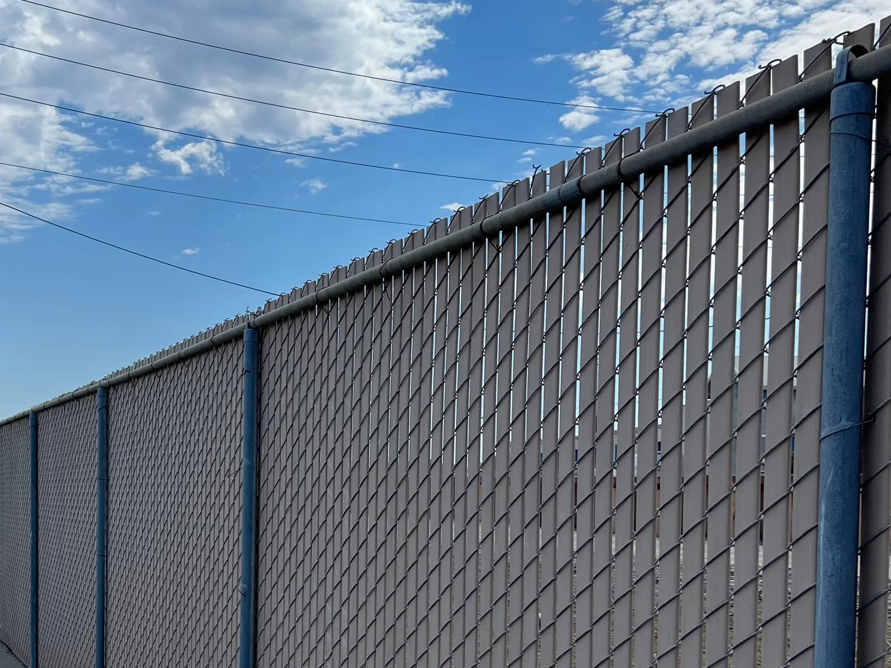 Long chain-link fence with white privacy slats along a commercial service lane