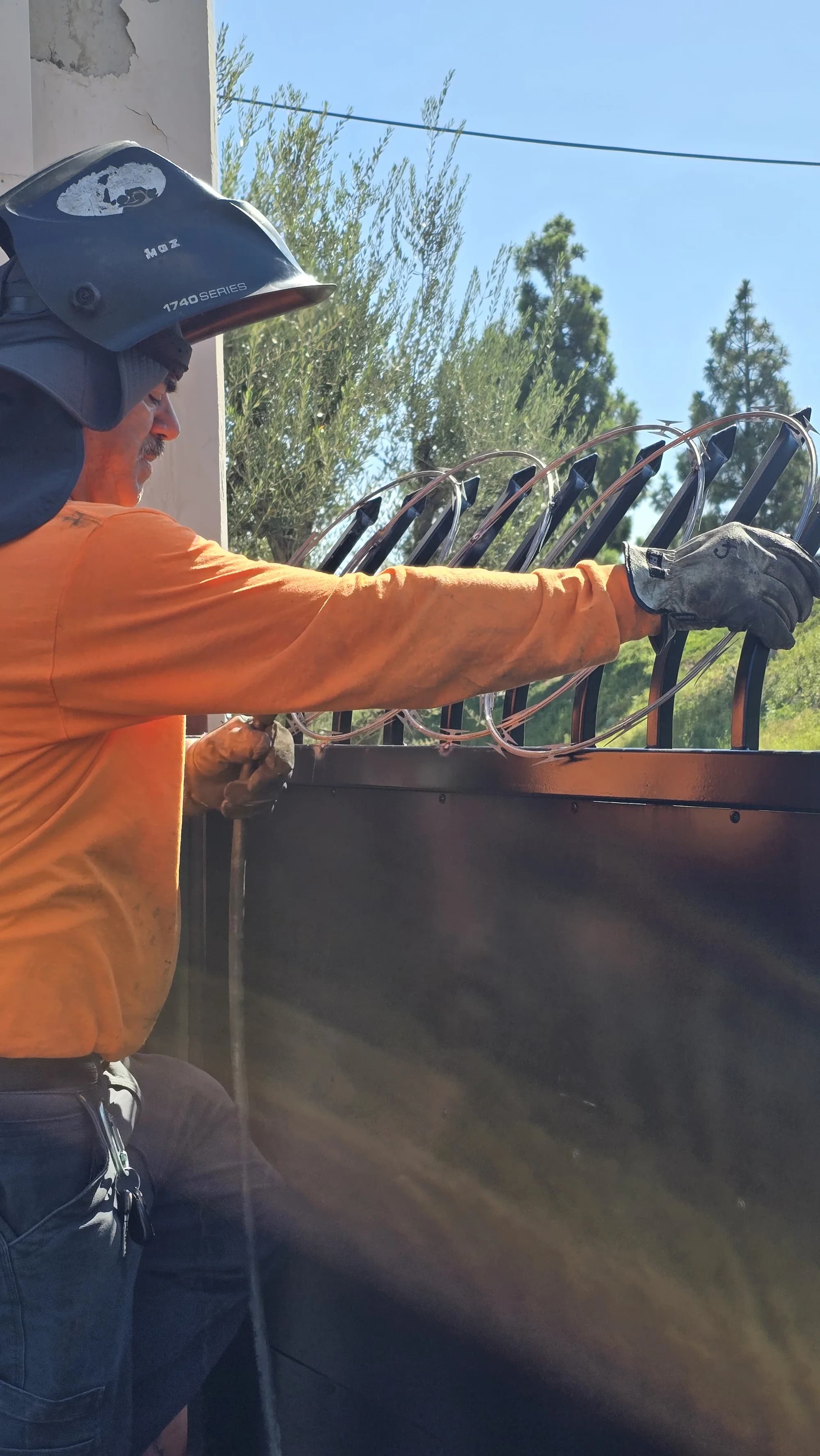 Fence worker working on the ornamental top of a large solid-infill security gate