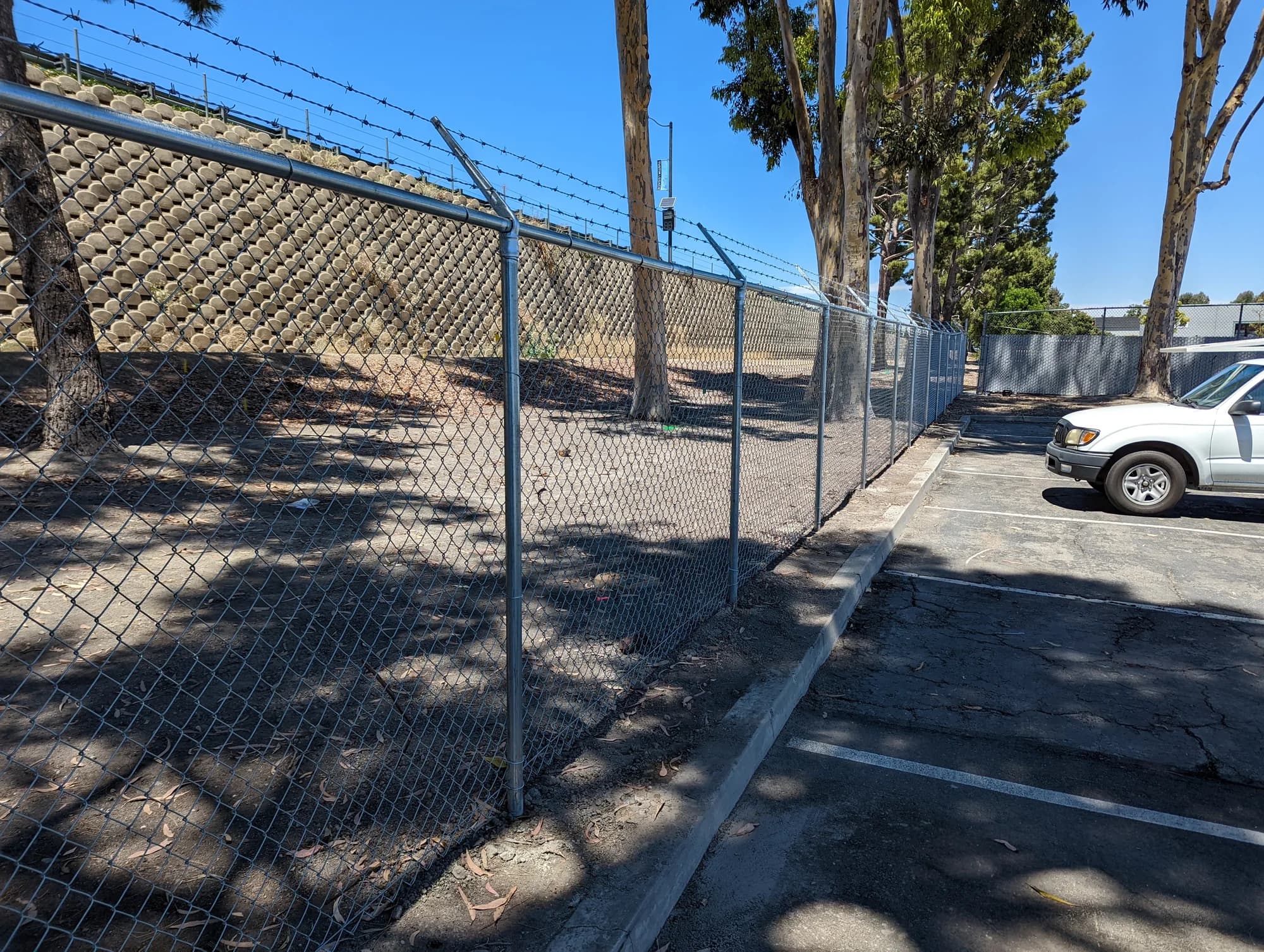 Galvanized chain-link security perimeter with barbed-wire arms beside a commercial parking area