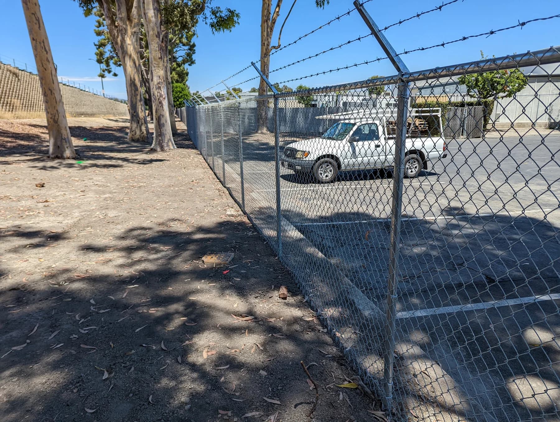 Chain-link and barbed-wire perimeter separating an embankment from a paved service yard