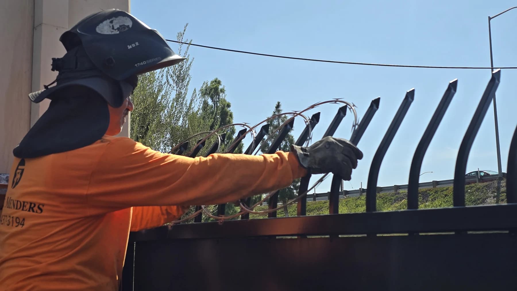 Fence Menders worker positioning ornamental anti-climb metalwork on a large commercial security gate