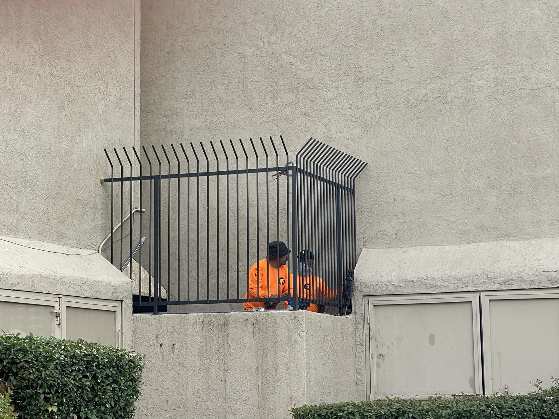 Two Fence Menders workers installing a black anti-climb security enclosure between commercial building walls