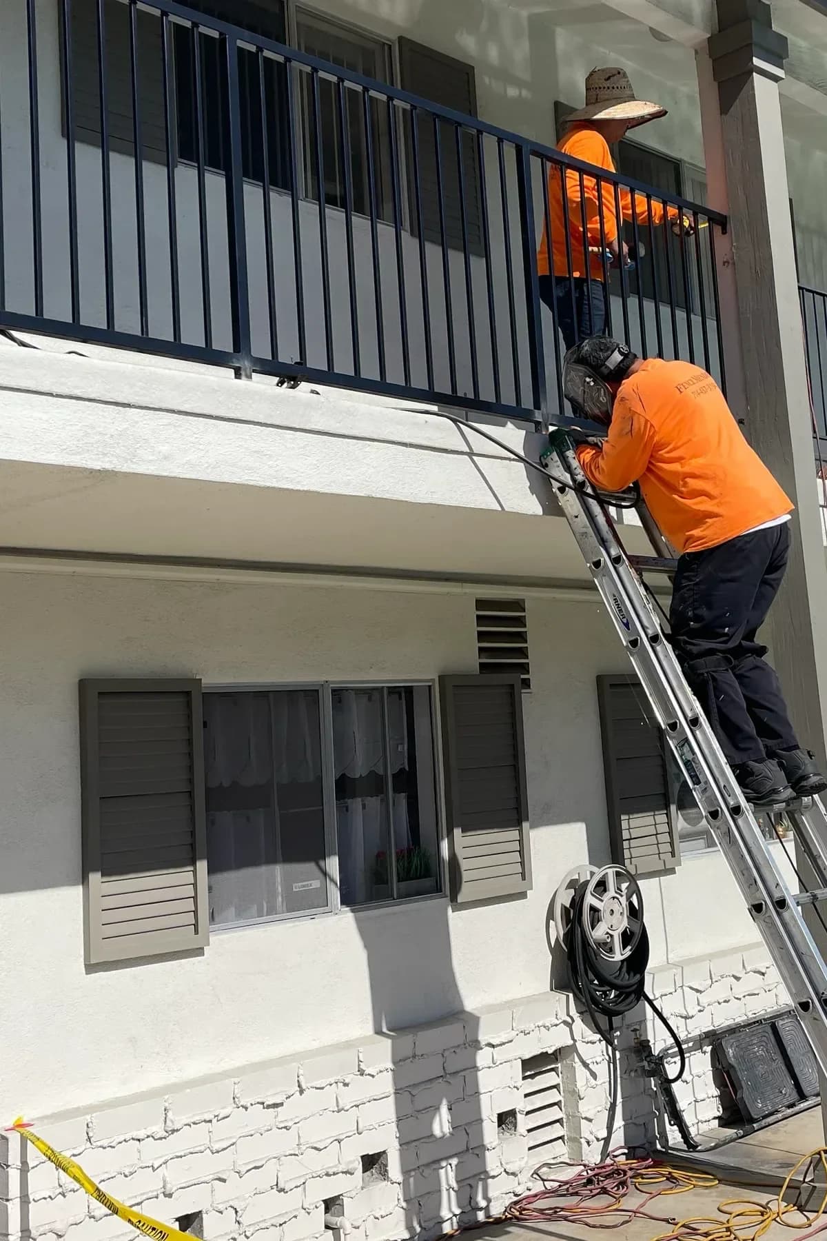 Two Fence Menders workers repairing an upper-level exterior corridor railing from a ladder