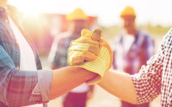 Workers handshake with gloves in a sunny outdoor setting.