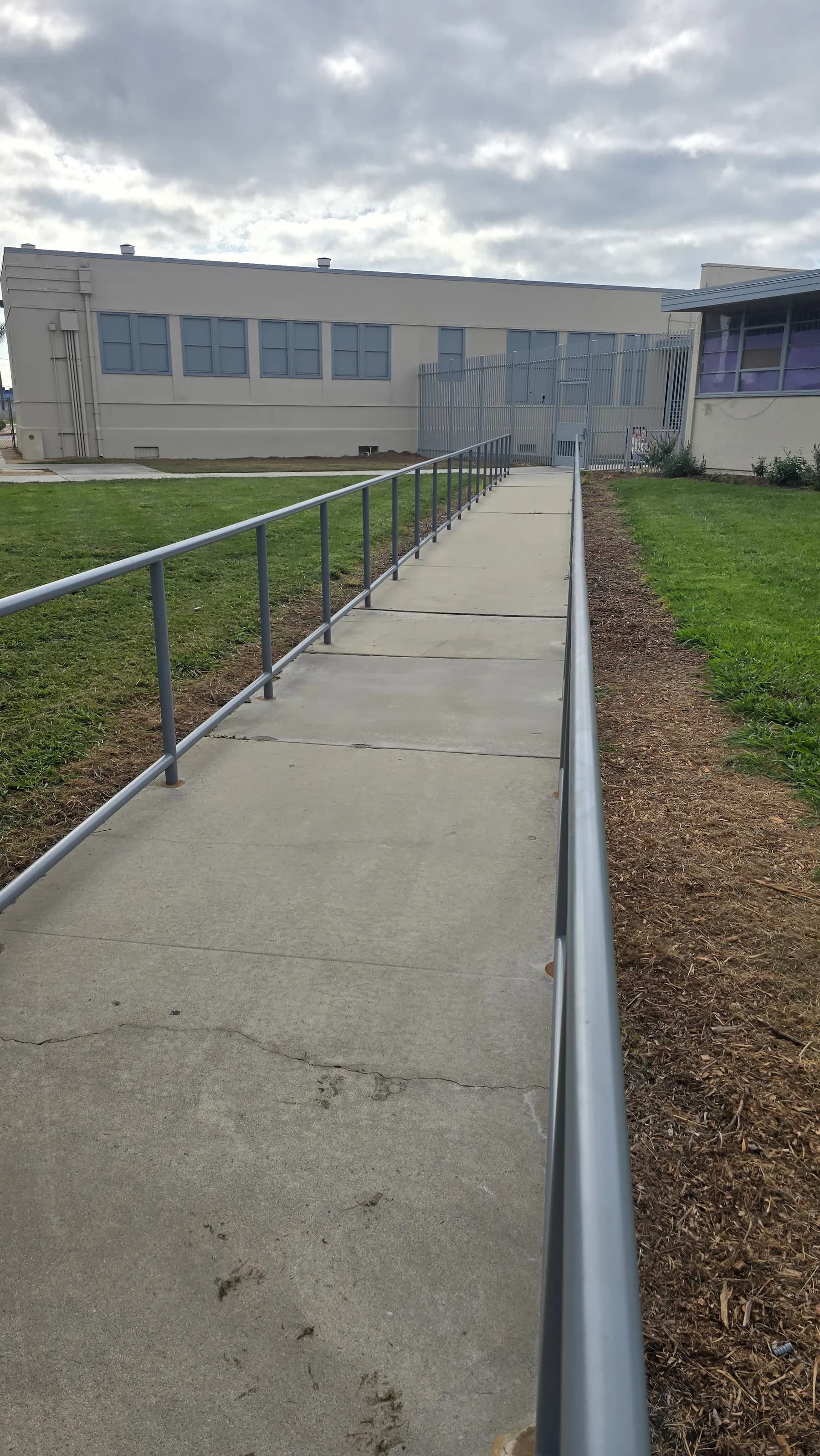 Long gray metal handrails along both sides of a paved exterior walkway