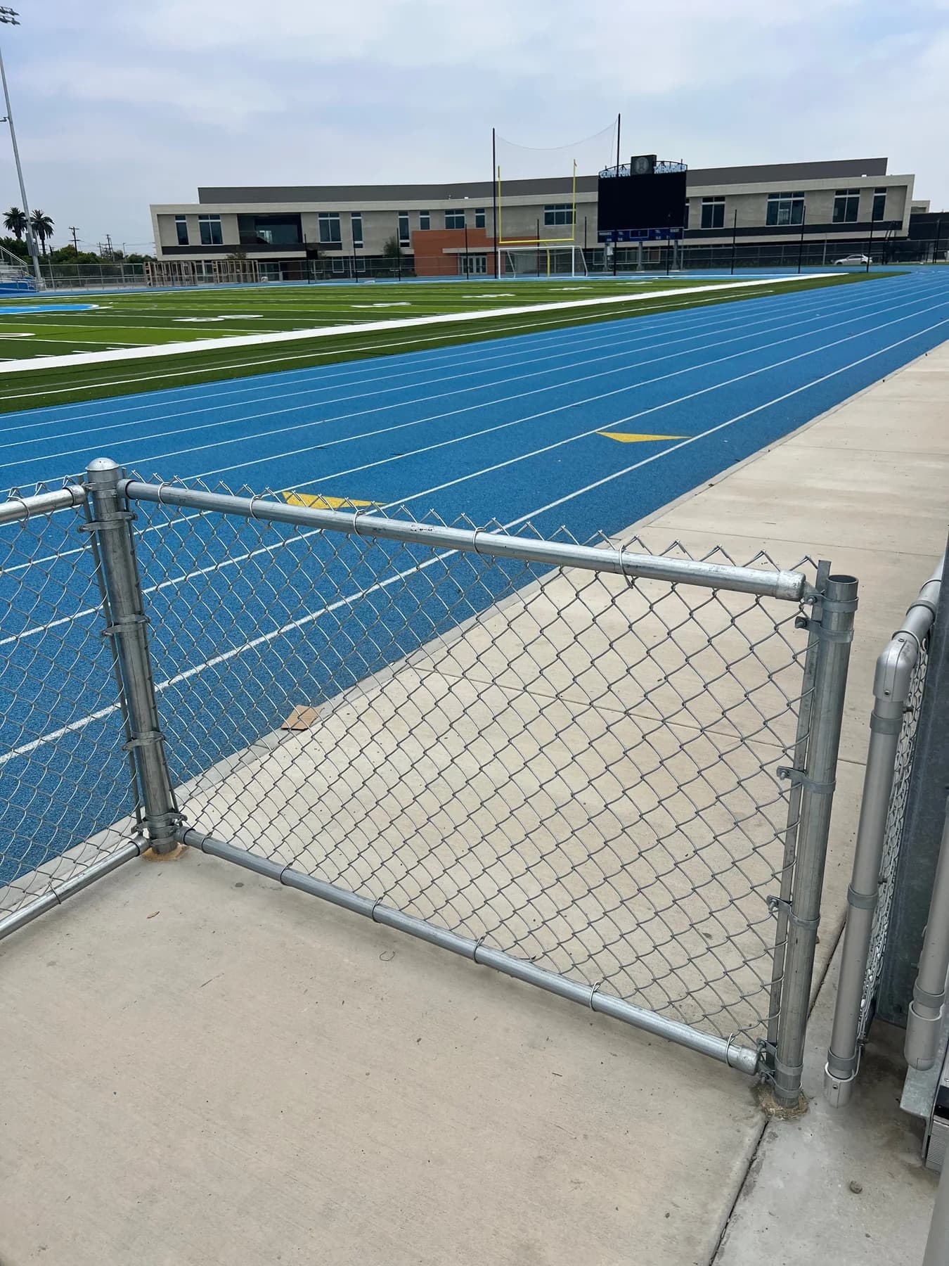 Chain-link access gate enclosing a blue running track and athletic field