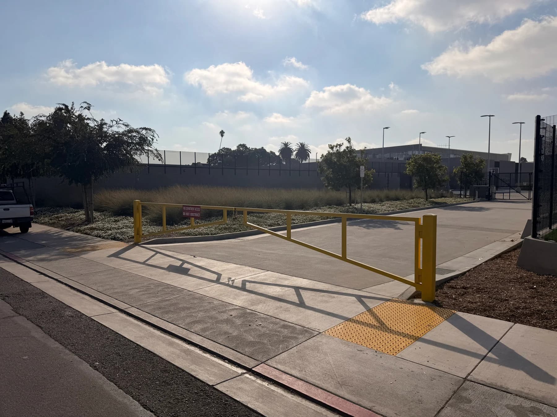 Yellow swing vehicle barrier controlling a paved access route beside an athletic field