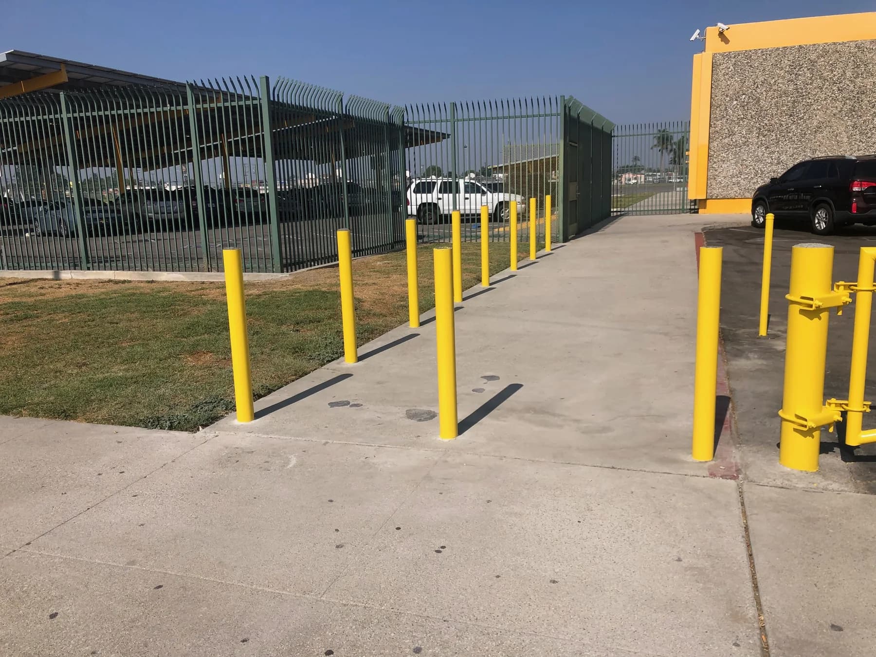 Tall black anti-climb security fence with inward-curved pickets beside a paved access lane