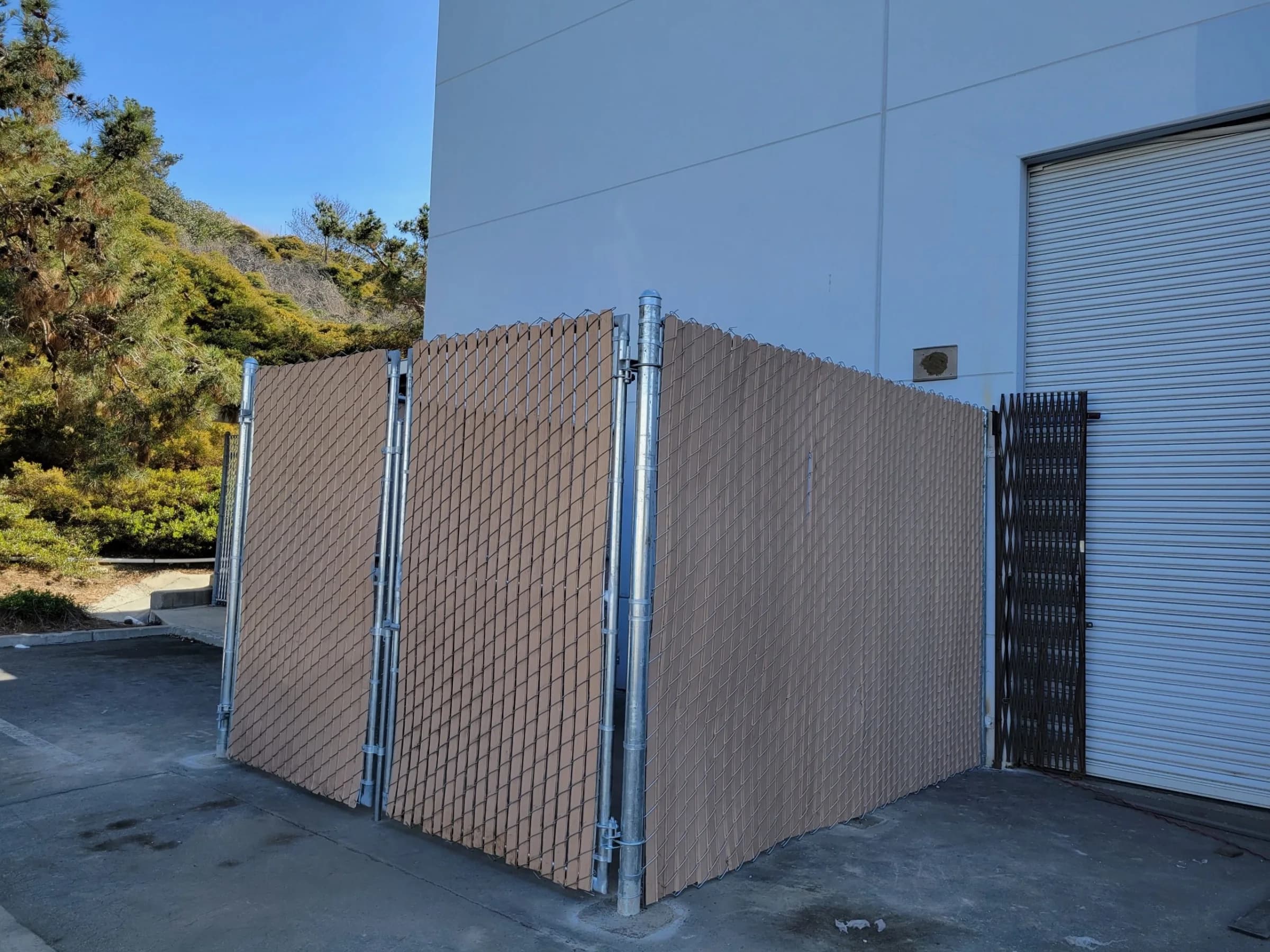 Chain-link equipment enclosure with tan privacy slats beside an industrial building