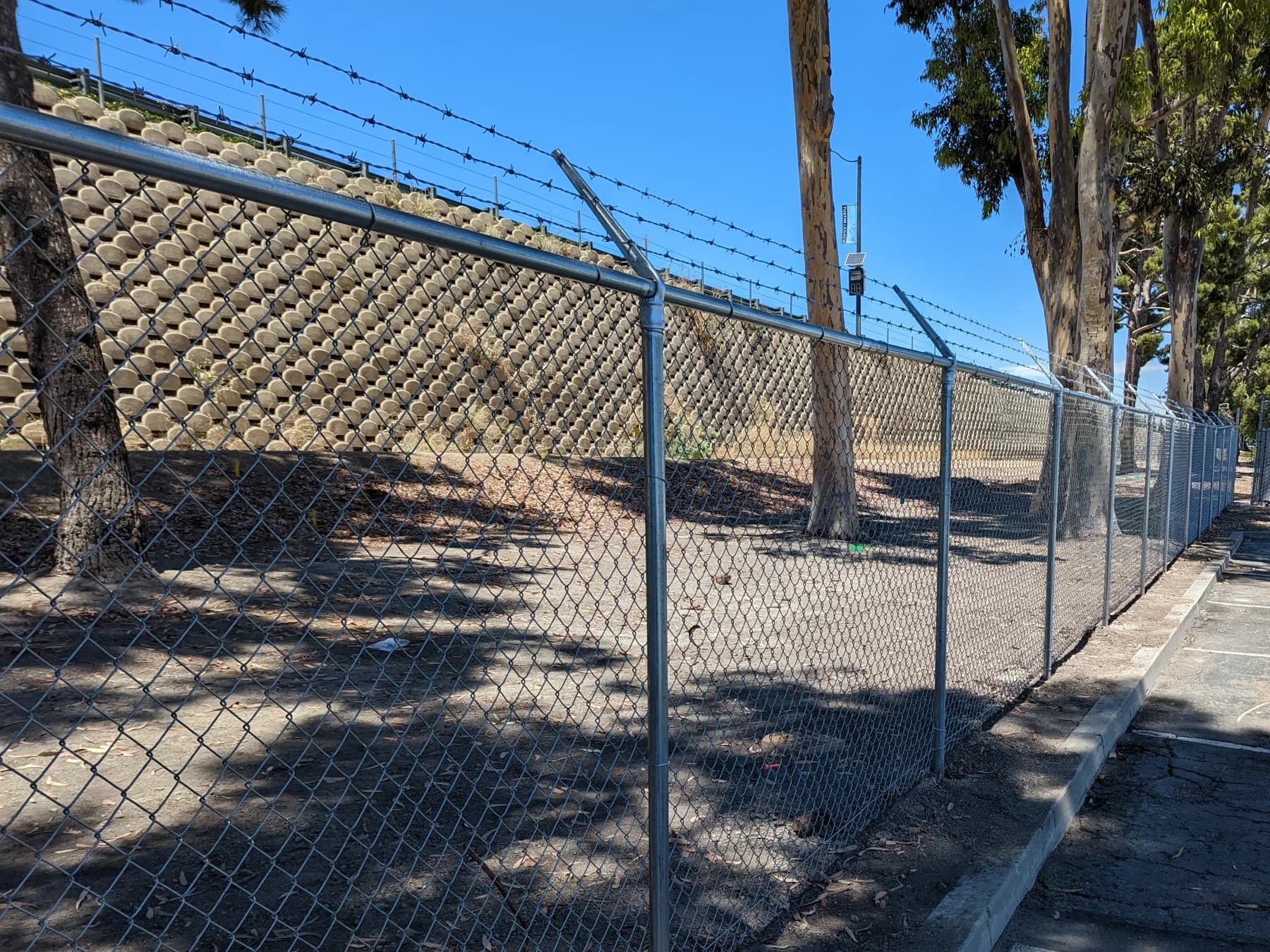 Galvanized chain-link security perimeter with barbed-wire arms beside a commercial parking area